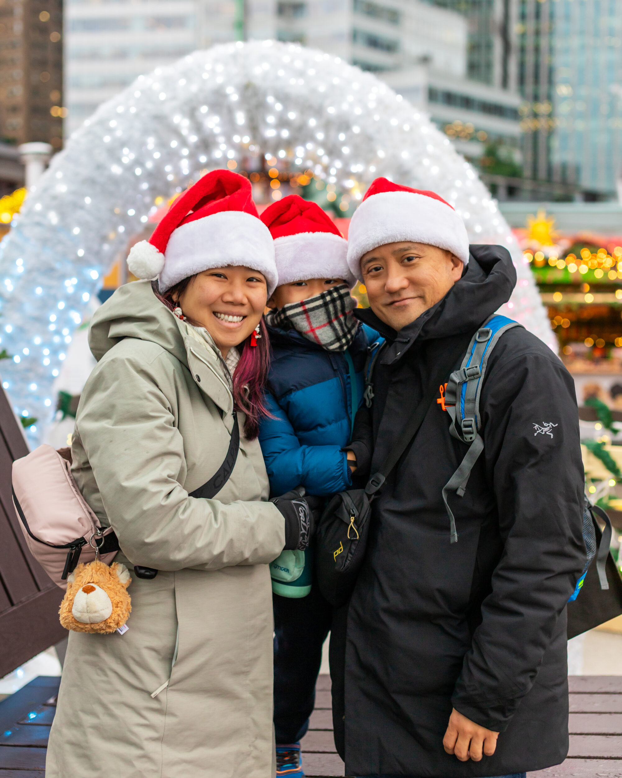 A three person family wearing Santa hats enjoying the Vancouver Christmas Market